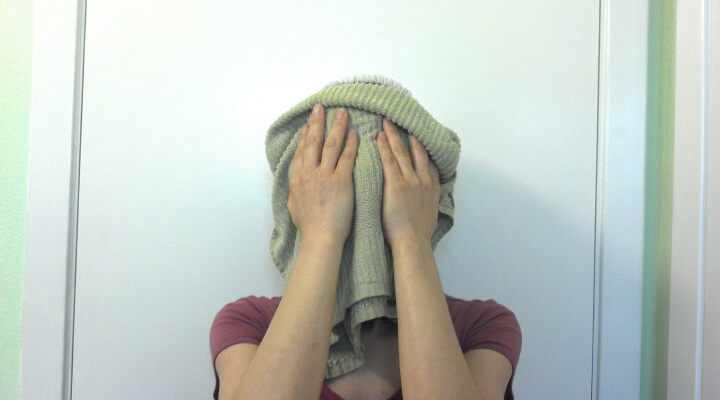 A woman holding green towel over her face.