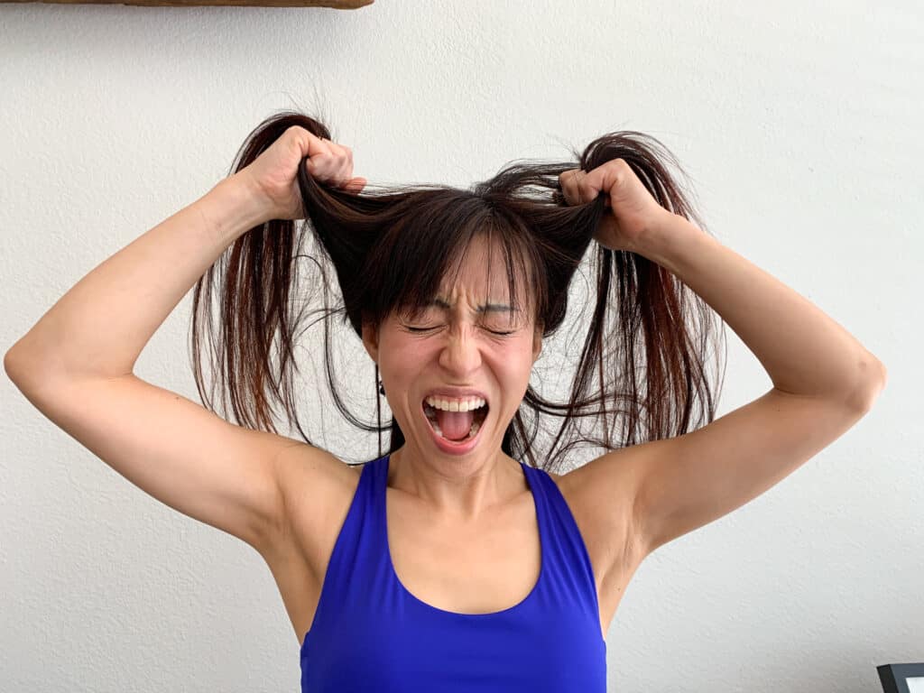 A stressed person yelling while holding its hair up. 