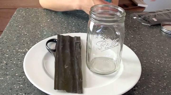 A glass jar, scissors and a black chocolate-like piece on white plate.