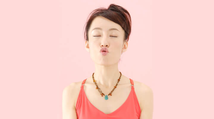 A woman with dark hair and in red sleeveless shirt holding her lips in O shape whit eyes closed.