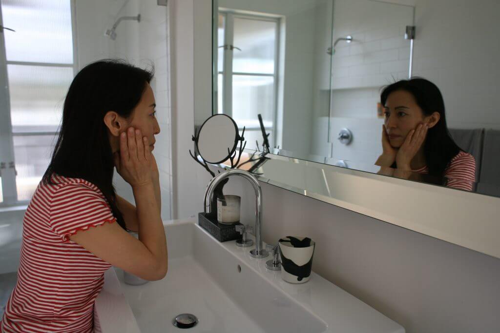 Fumiko Takatsu looking at the mirror and touching her face. 