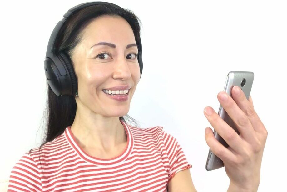 Woman with black hair with headphones on the head and a cellphone in the hand looking at the camera. Fumiko Takatsu on using earbuds and their benefits for symmetrical face. 